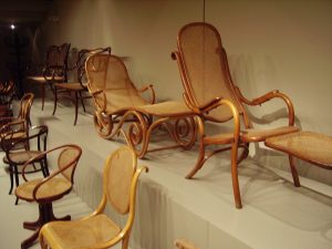 一张Thonet在仓库般的背景下的弯曲木椅的照片。椅子是轻木制的，有编织的座椅和靠背。