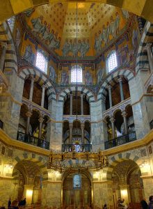 亚琛帕拉廷教堂:教堂的圆顶天花板的照片。有两排拱门，顶部有迷你拱形窗户。此外，天花板的顶部是金色的，上面有各种宗教形象。