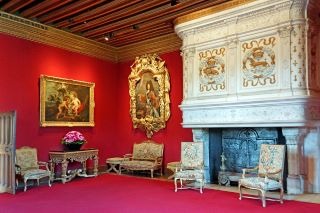 Castillo de Chenonceau. Salón de Luis XIV con profundas paredes rojas, cornisas de oro, una grande chimenea blanca y sillas de color claro alrededor de la habitación. Esta habitación contiene muebles que el entonces propietario del castillo recibido del Rey Luis XIV, junto a un retrato del rey.