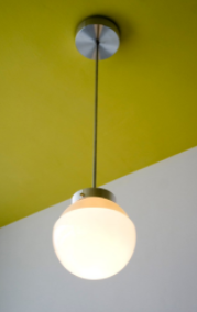 Lampada da soffitto HMB 29: una semplice lampada in metallo, con una lampadina gialla appesa a un bastone di metallo.