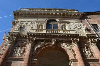 卡皮塔尼亚托宫自下而上的照片。中间有一个拱形，下半部分是锈粉色，而顶部是棕褐色。有各种各样的装饰品组成了这个结构。