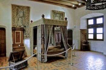 亨利二世的房间:一张豪华的天篷床位于中心，两边都有挂毯，房间右侧有一扇窗户和一把椅子。