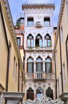 一条小巷的照片，在尽头有一个高而瘦的建筑，有三层哥特式的窗户。位于意大利威尼斯。