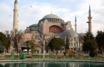 伊斯坦布尔的圣索菲亚大教堂:一座巨大而华丽的建筑，周围有各种圆顶和4座细细的塔楼。此外，在照片的前景中有一片水域。