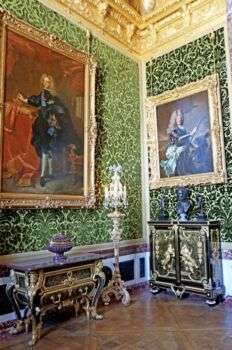 房间的墙壁是绿色的，有两个金色的相框，上面挂着宏伟的肖像，还有带有金色基调的深色家具。此外，天花板似乎也是金色的。