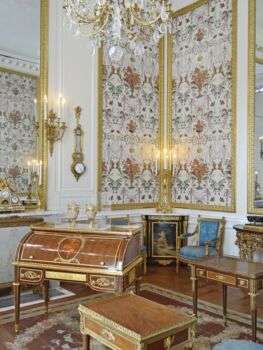 一个白色墙壁的大房间，房间里有金色的木制家具。