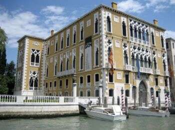 卡瓦利-弗兰凯蒂宫的照片，这是一个巨大的矩形结构，坐落在威尼斯大运河沿岸。此外，该结构是芥末色，白色拱形窗户和各种装饰。