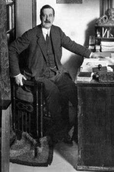 Portrait of Behrens in black and white. Additionally, he is sitting down at a desk.