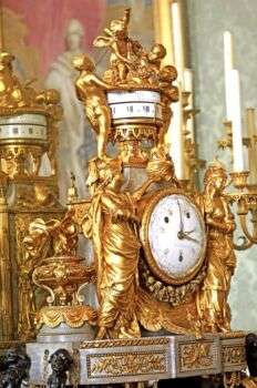 一座华丽的金色大钟，有不同的角度，白面大钟周围环绕着女性雕像。