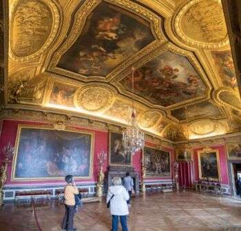 一个宏伟的房间，红色的墙壁，巨大的复杂的画，金色的天花板上有三幅宏伟的画。