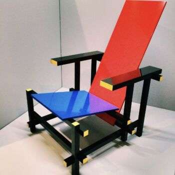 Red Blue chair (1917-1918) by Gerrit Rietveld: A red-backed chair with a blue and purple seat. Additionally, the legs and arms are black with yellow accents on the edges.